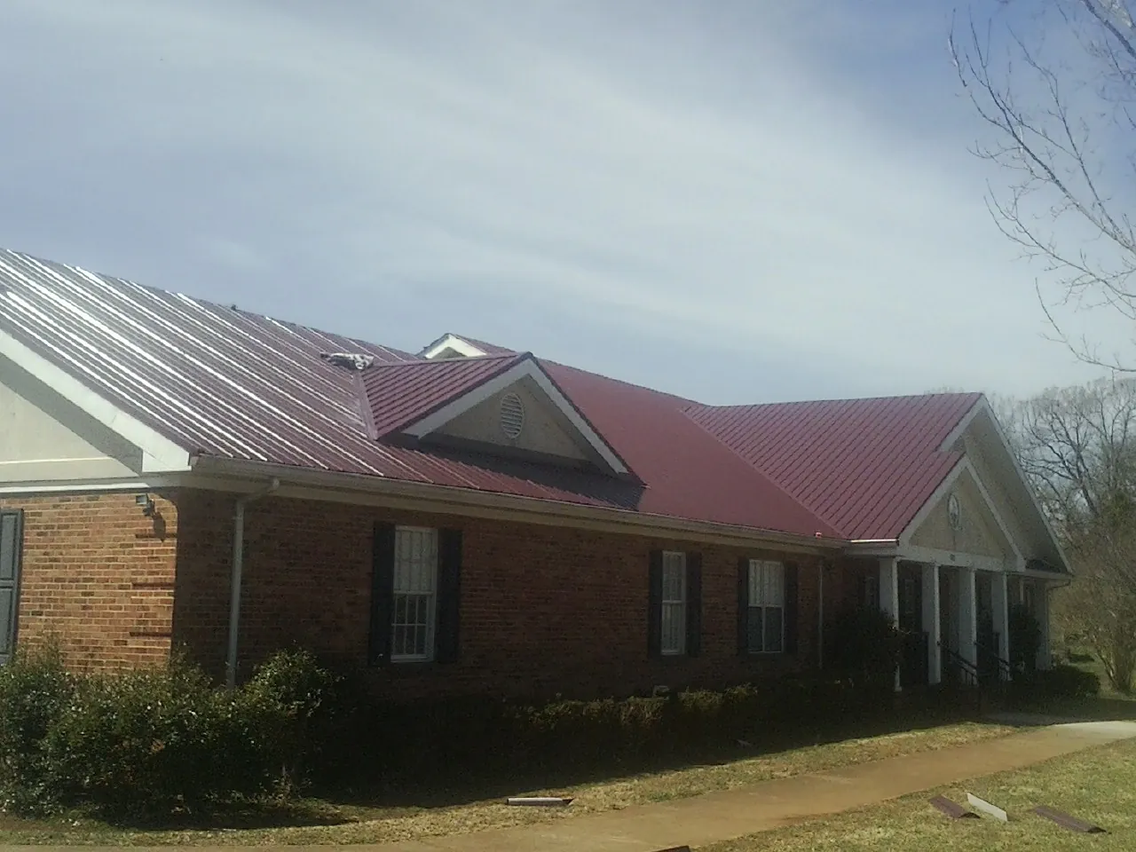 Red metal roof with gabled entries on a long brick building, from a Hail Damage Roof Repair job in Sun City